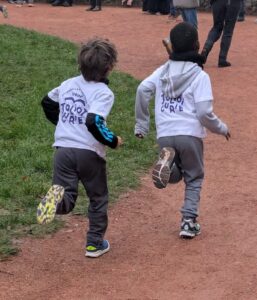 Deux enfants de dos avec un t shirt à l'effigie de l'école Irène Joliot Curie sont en train de courir dans le parc de la mairie.